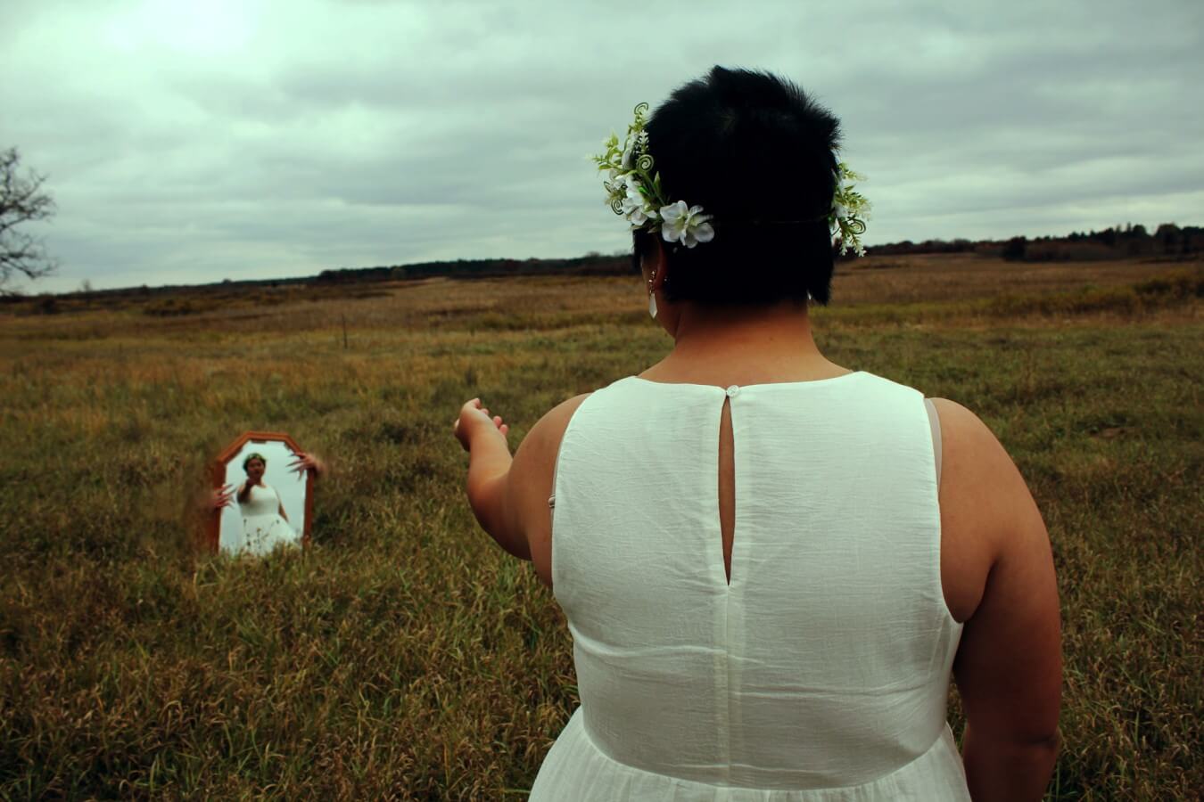 A person reaching their hand out to a mirror in a grass field.