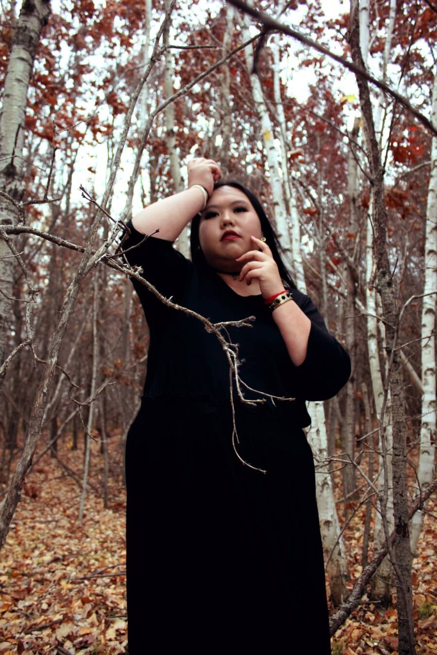 A black witch standing in the middle of a red birch forest.